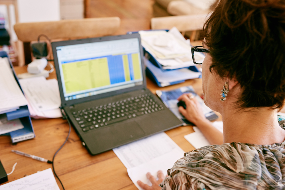 over the shoulder shot of a mature business woman wearing glasses busy working on her new notebook in her home office