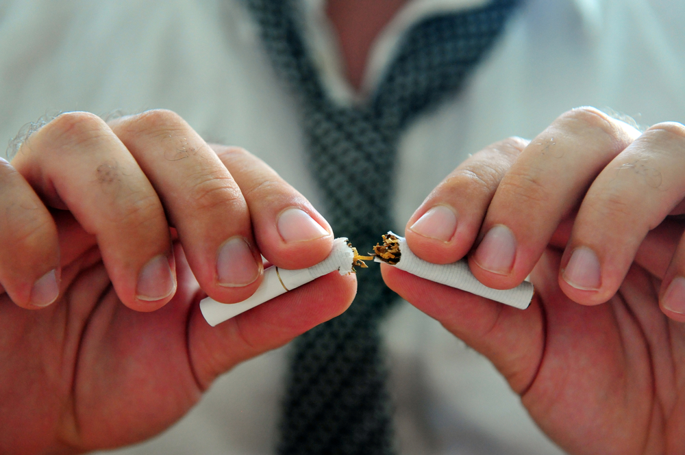 Concept photo of a man quitting smoking by breaking a cigarette.