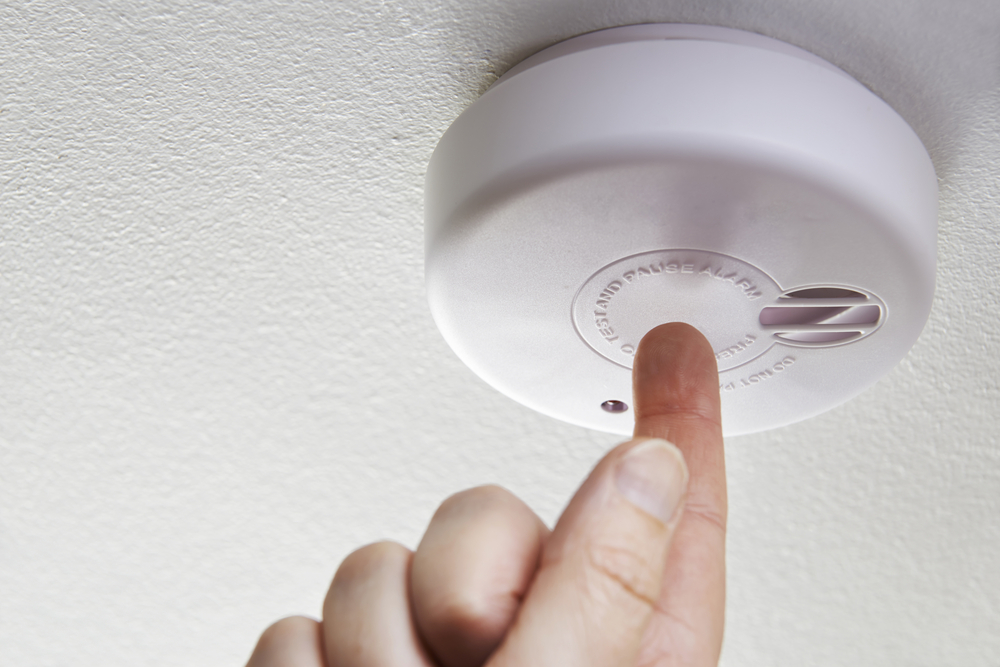 Close up of a hand testing a domestic smoke alarm.