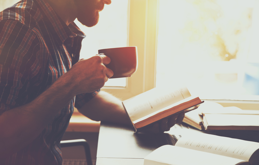 A bearded man reading books and drinking coffee.