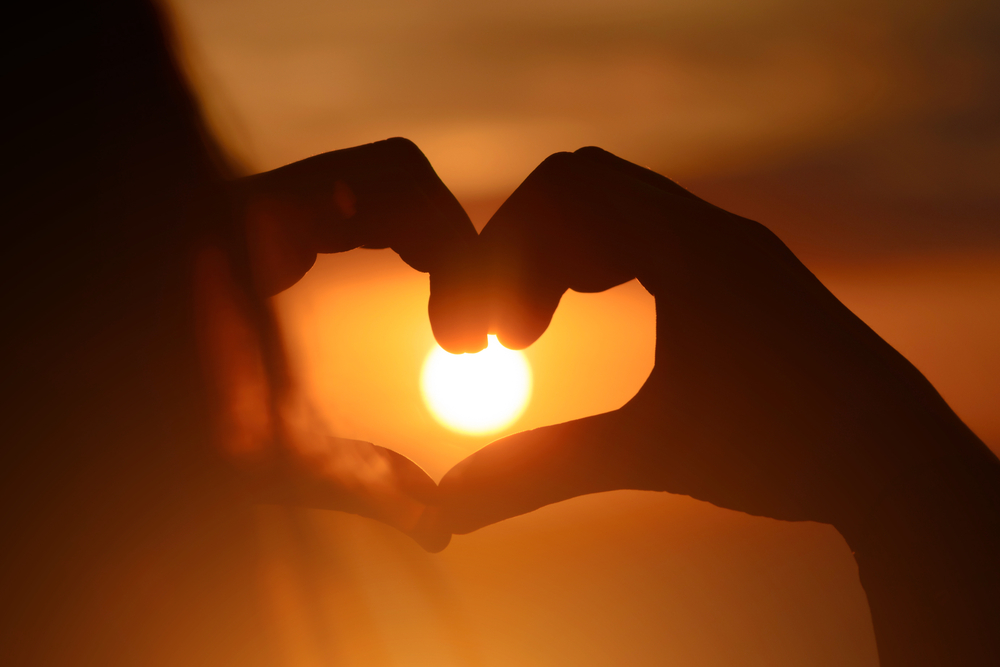 A girl holding her hands up in a heart shape during a sunset.