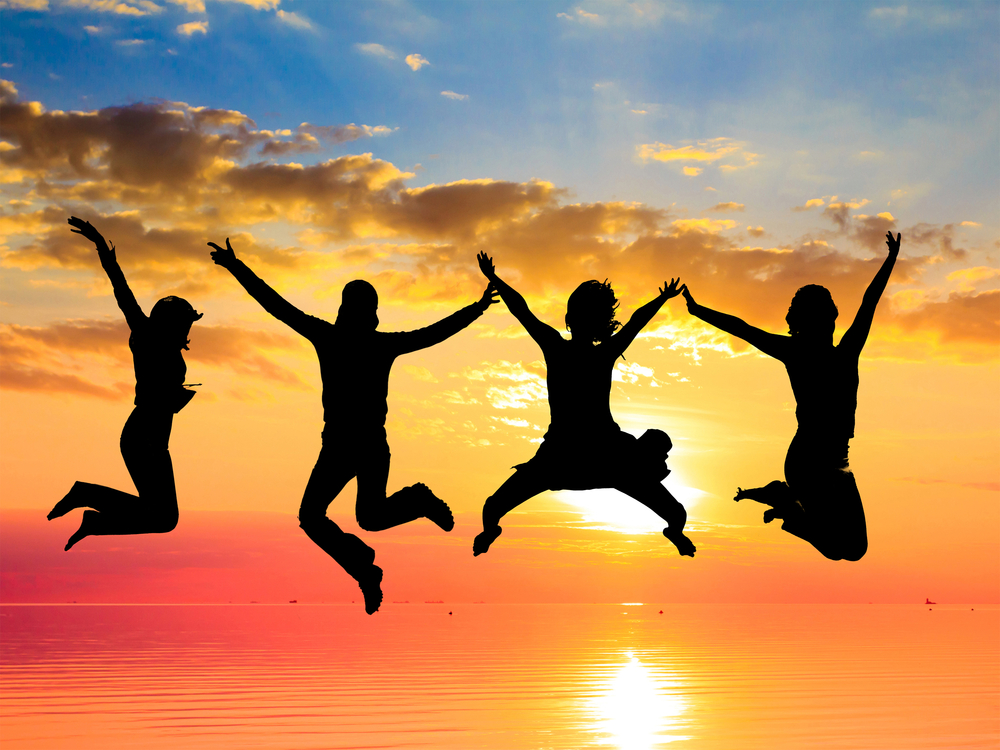 A group of people jumping who are backlit against a sunset.