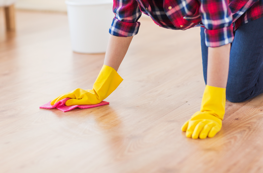 A person on their hand and knees scrubbing the floor with yellow gloves.