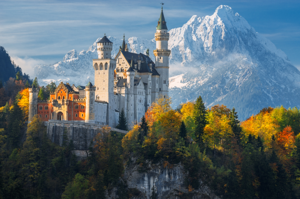 Germany. Famous Neuschwanstein Castle in the background of snowy mountains and trees with yellow and green leaves.