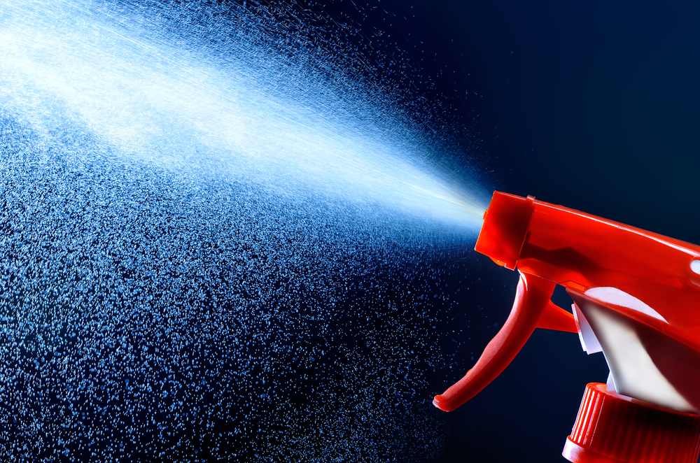 A spray bottle shooting water over a dark background.