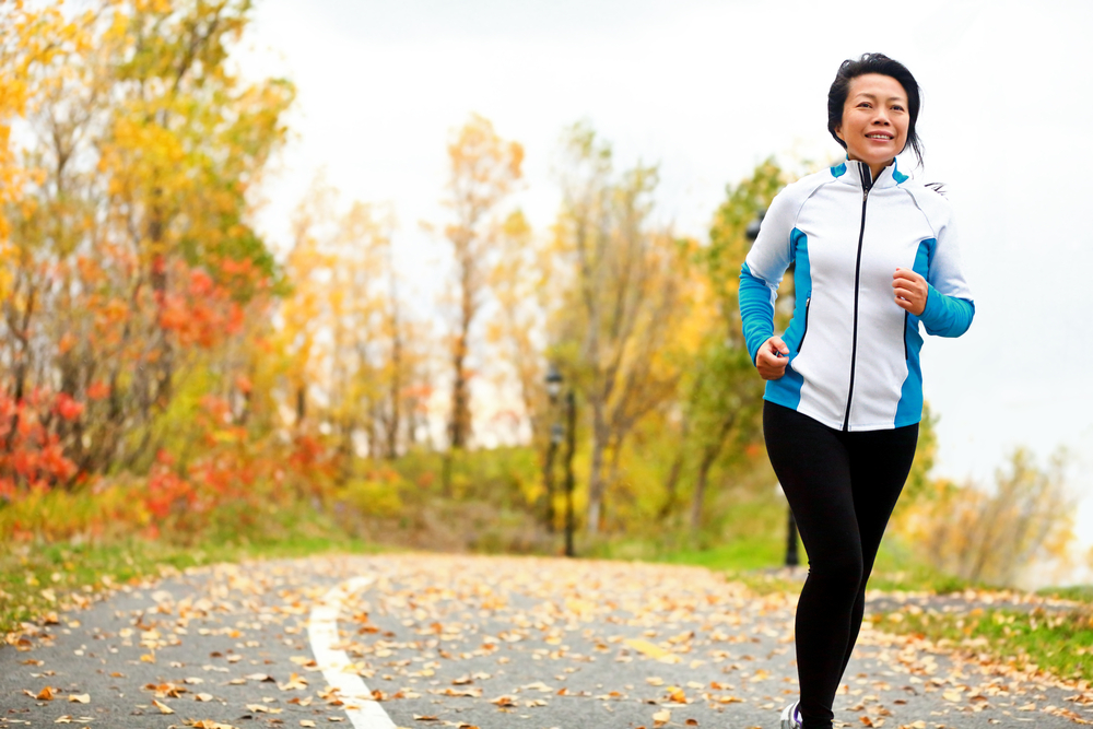 A mature woman jogging with fall foliage in the background
