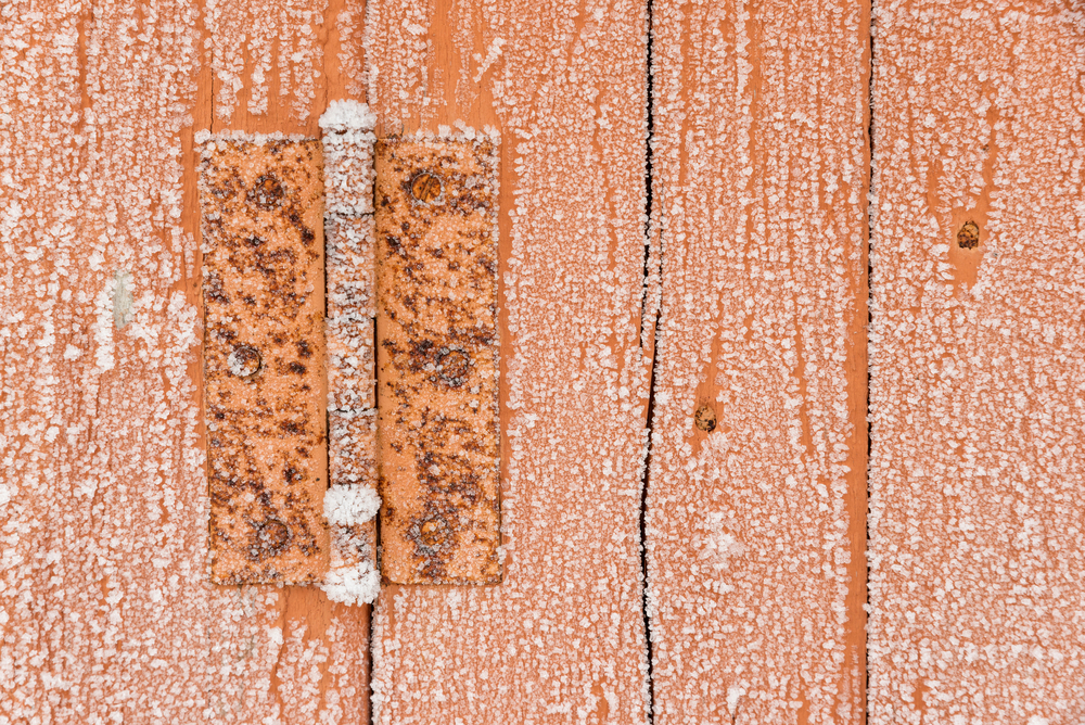 Rusty hinge on a frozen wooden old door in the winter with snow flakes on it as a rustic background.