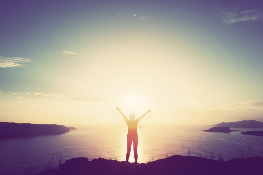person standing on a cliff waving arms in air freedom