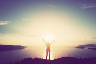 person standing on a cliff waving arms in air freedom