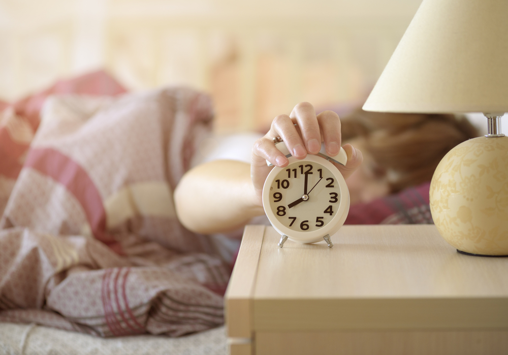 Person in bed turning off alarm clock on side table