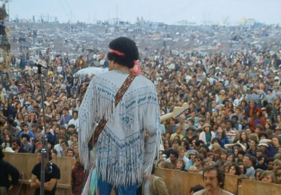 Jimi Hendrix performing to a huge outdoor crowd at the music festival Woodstock. 