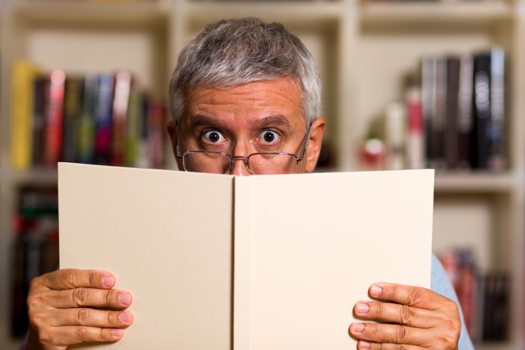 Man reading a book with a bookcase background.