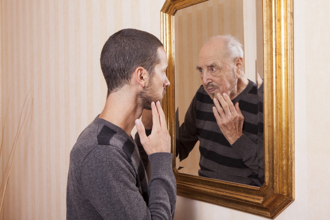 A young man looking into the mirror and seeing his aged reflection.