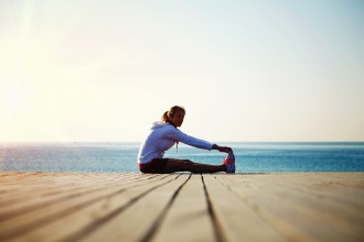 A female jogger stretching on a dock.