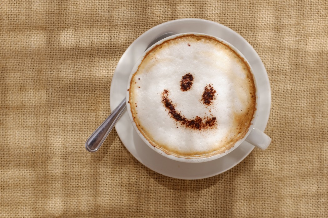 Coffee cappuccino with foam or chocolate smiling welcome happy face in restaurant or hotel.