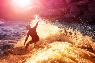 A surfer riding a wave at sunset.