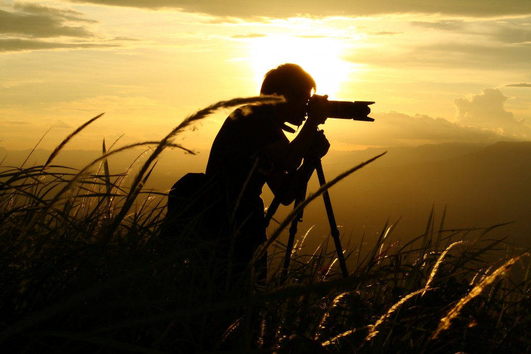 A silhouette of a man taking a photo during sunset or sunrise.
