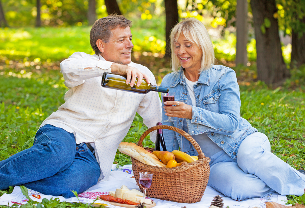 A man pouring a glass of wine into a woman's glass on a picnic.