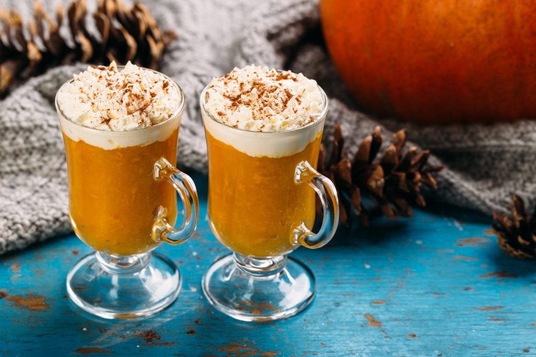 Pumpkin spiced latte or smoothie with whipped cream in glass on blue background Autumn or winter hot drink.